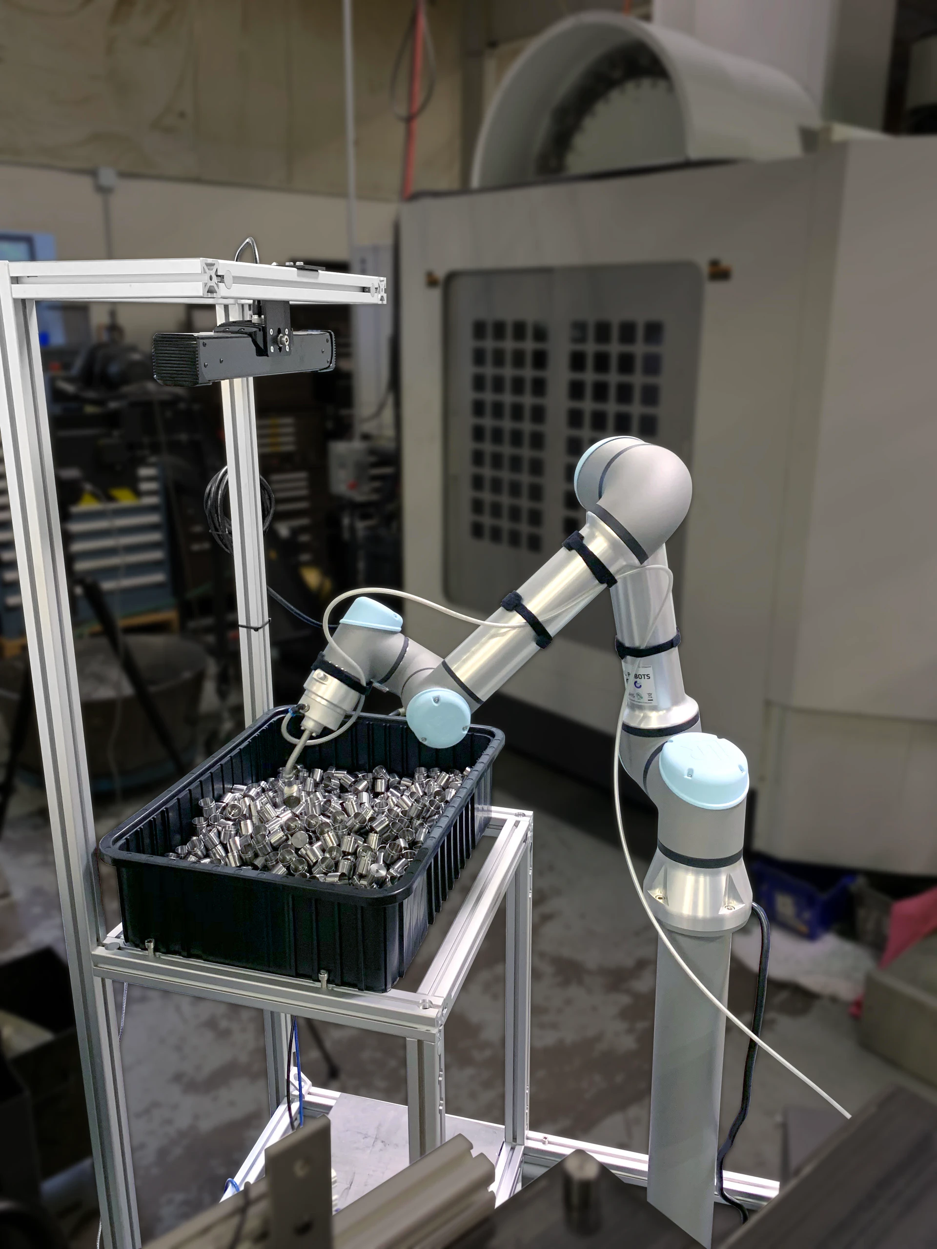 Industrial robotic arm reaching into a bin of small metal parts in a workshop setting