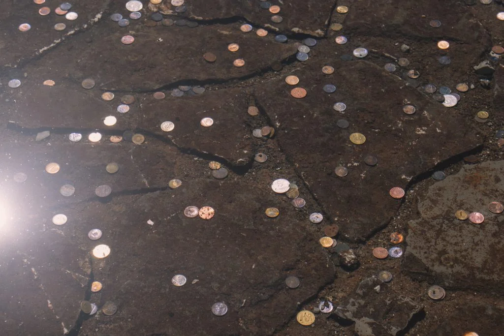 Close-up of scattered coins on a cracked stone surface with reflective highlights