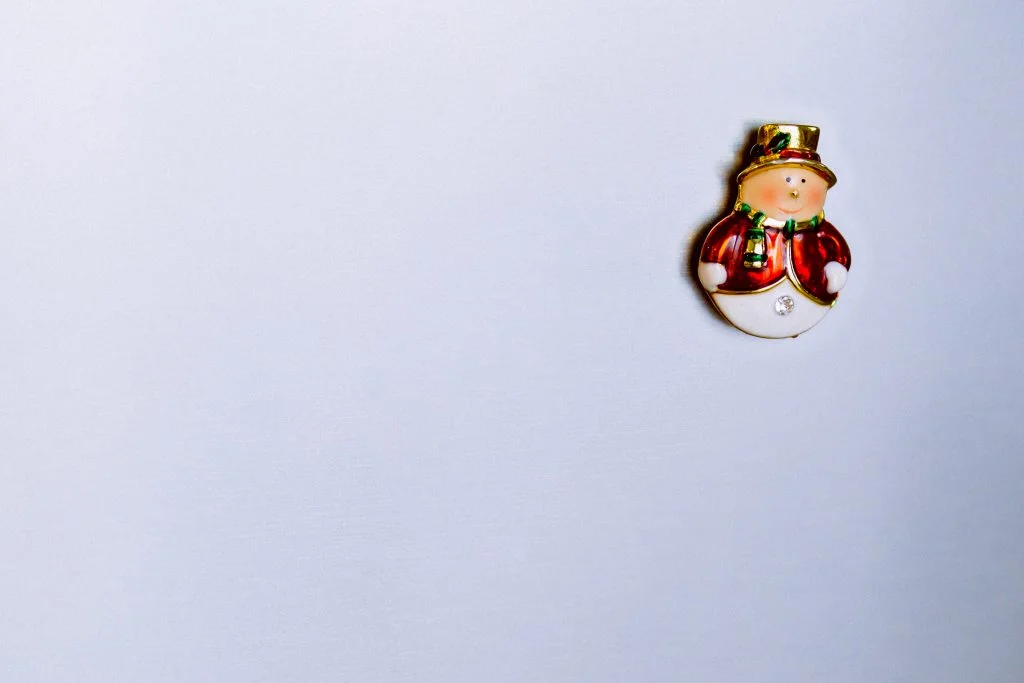 A small decorative snowman ornament in red white and gold against a light blue background